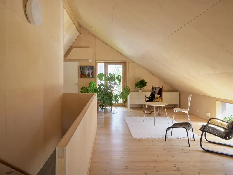 Upper floor plywood-lined space with sloped ceiling and potted plants near the window