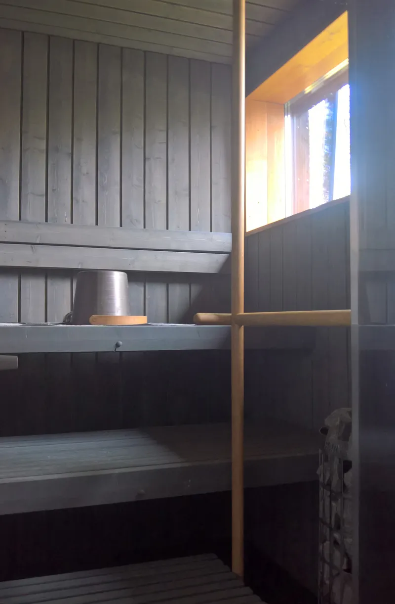 Darkened sauna interior with timber benches and light filtering through a window opening