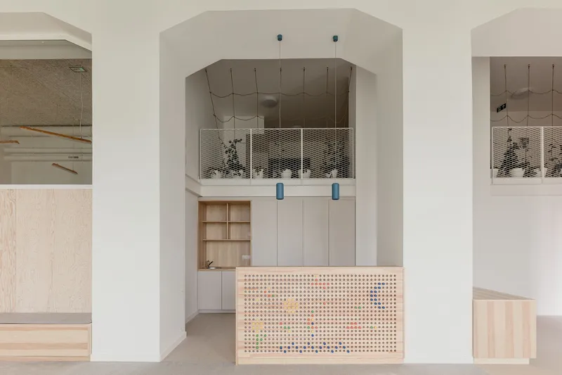 Reception counter with pegboard facade and colorful pegs beneath an arched opening and mezzanine with mesh balustrade