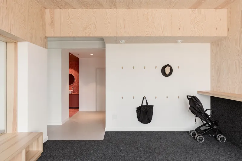 Entry corridor with plywood ceiling, white peg wall holding bags and a stroller, and view to red tiled room beyond