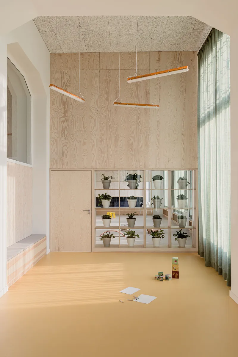 Double-height space with plywood wall cladding and open shelving displaying potted plants behind glass