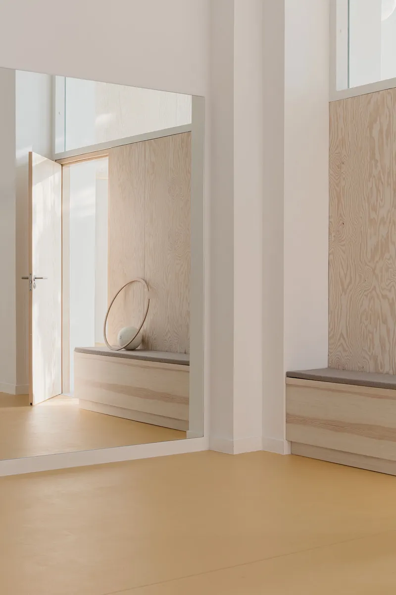 Corner nook with built-in plywood bench and round mirror reflecting white doorway and yellow flooring