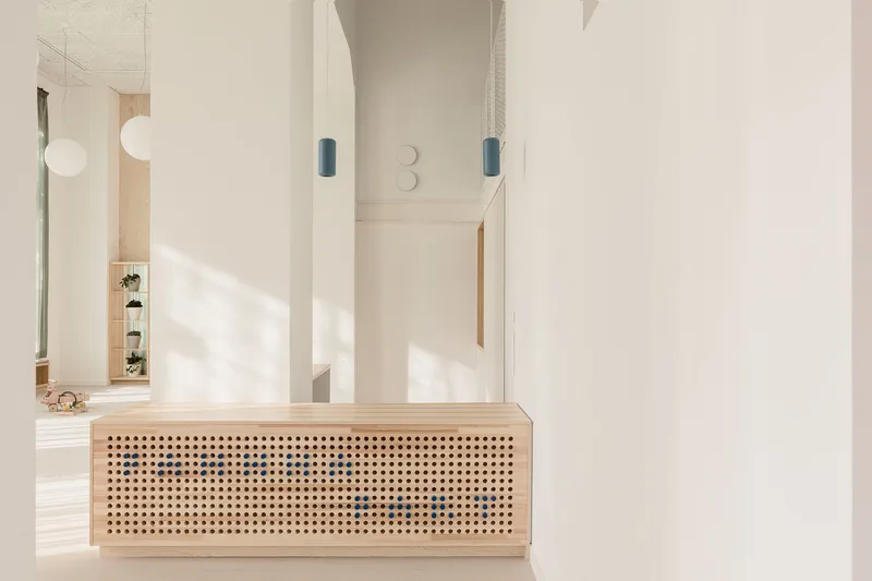 Plywood reception counter with perforated screen panel lit by blue pendant lights in white hallway