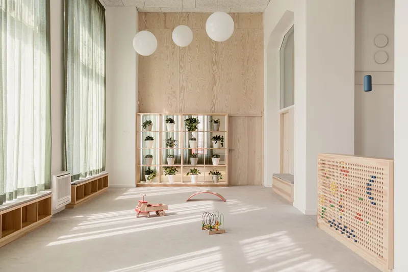 Double-height playroom with plywood plant wall, sphere pendant lights, and sheer curtains filtering daylight
