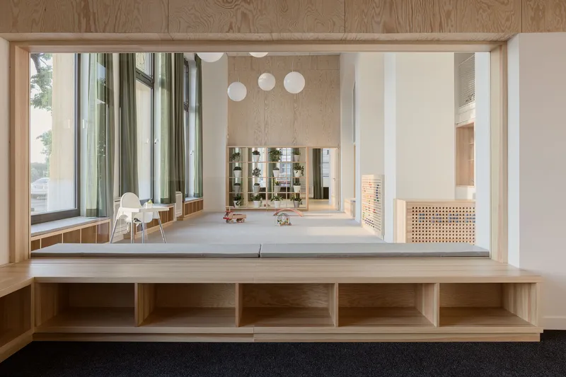 Oak framed window opening from upper level overlooking a double-height playroom with pendant lights and floor-to-ceiling windows