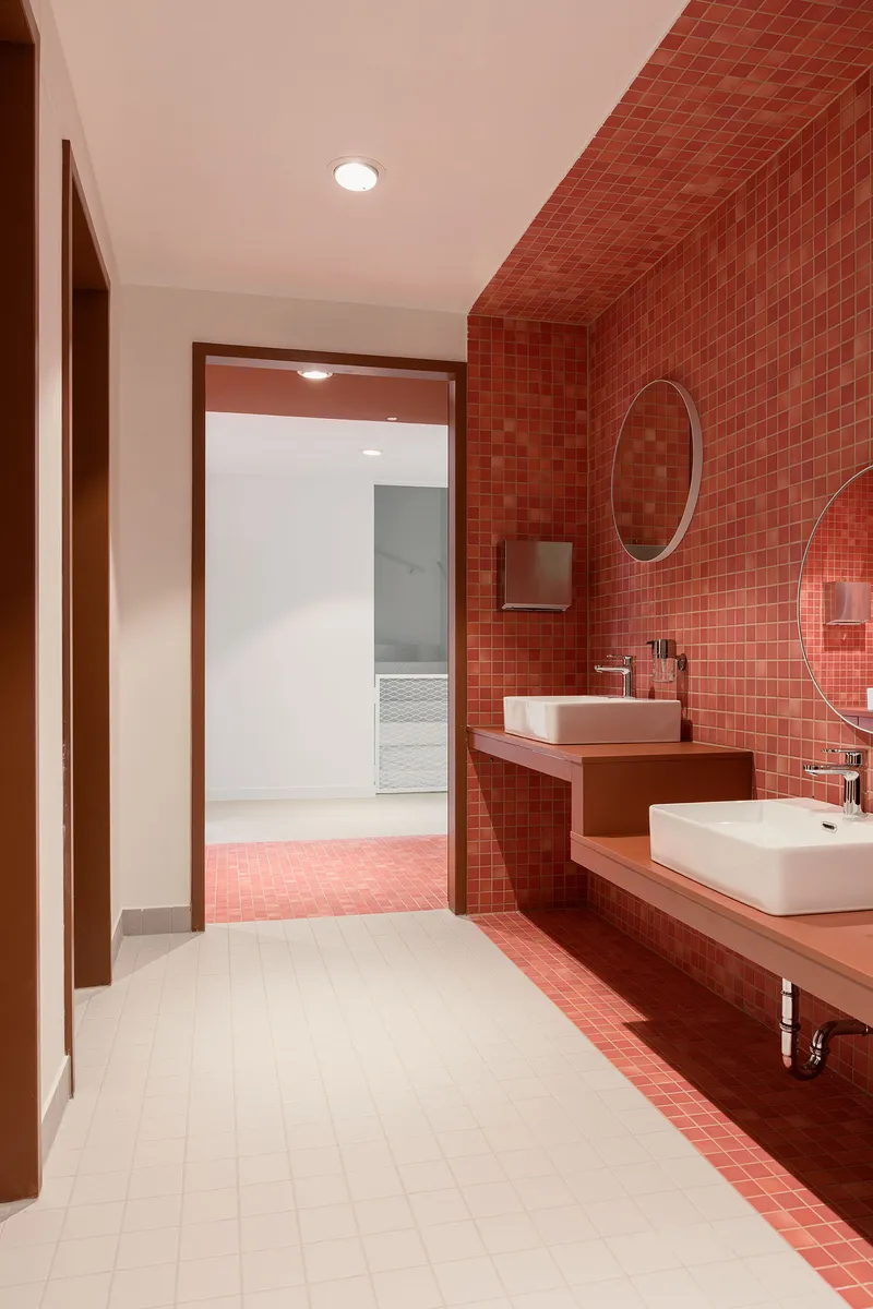Bathroom with terracotta tile walls and ceiling, white vessel sinks and circular mirror over shelf