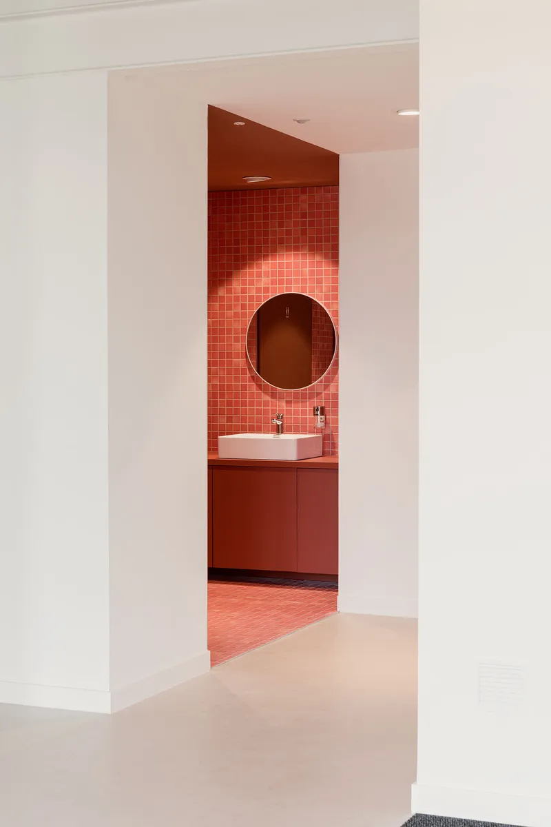 Doorway framing a terracotta-tiled bathroom alcove with circular mirror and white vessel sink