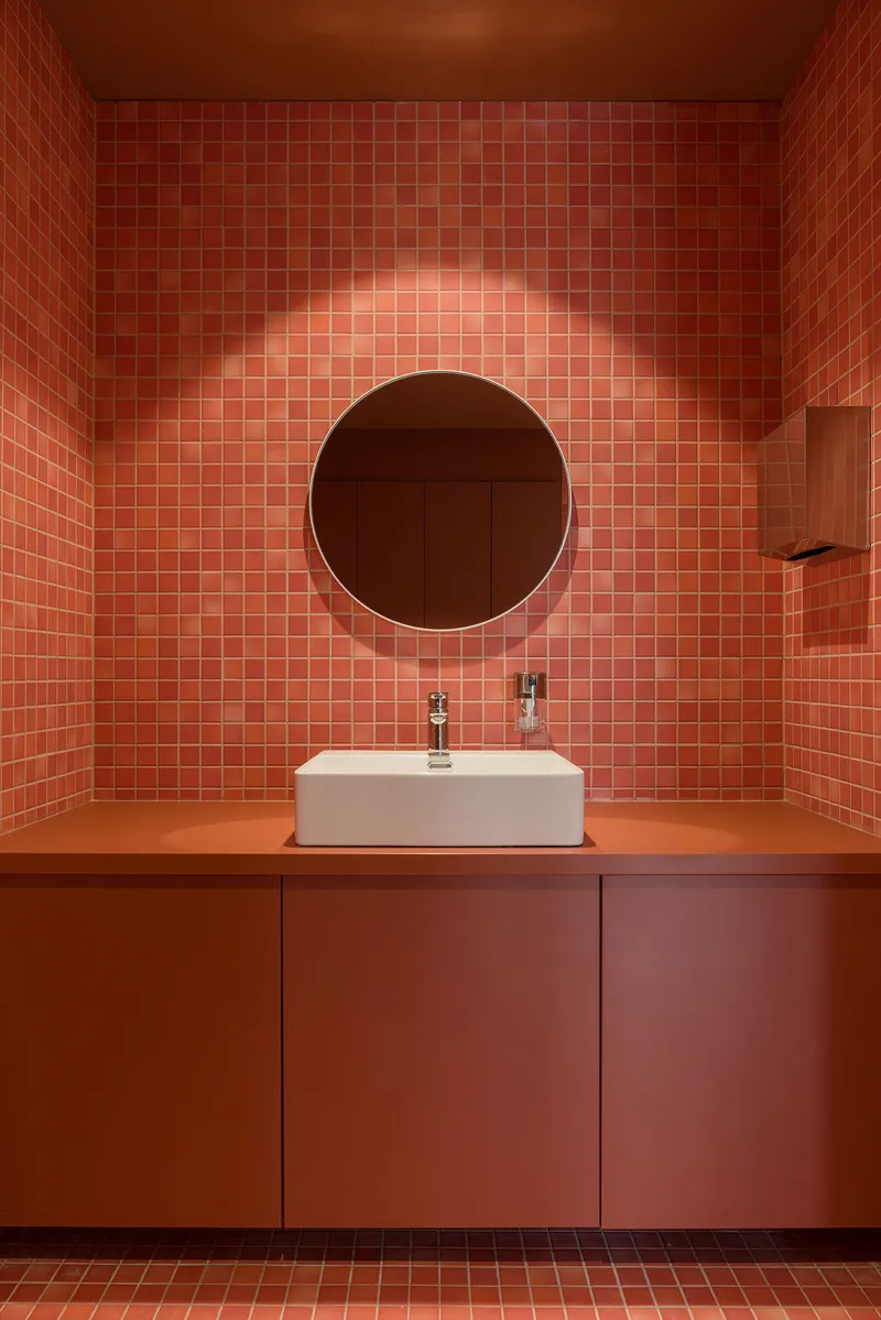 Terracotta tile vanity wall with backlit circular mirror above white vessel sink on orange countertop