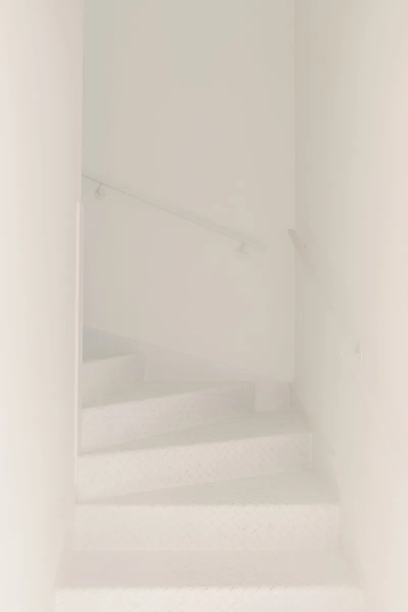 White plastered staircase with thin metal handrail ascending through a narrow enclosed stairwell