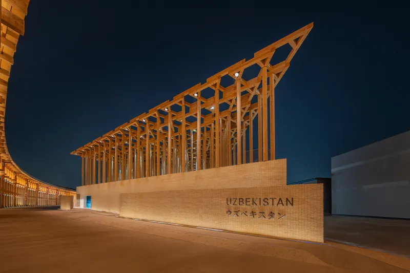 Timber canopy with angled slats rising above a sandstone wall at dusk