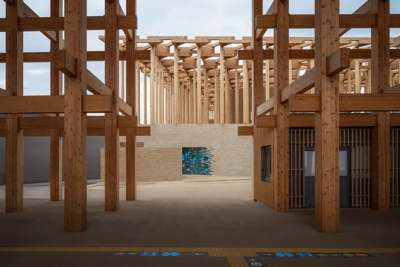 Interior view through timber post-and-beam structure with a blue glazed tile installation in the beige brick wall