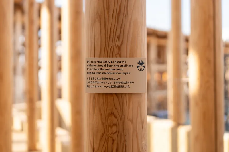 Informational tag attached to a timber column with bilingual text about wood origins