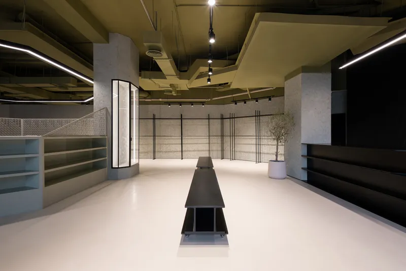 Interior retail space with white resin flooring, glass-framed columns, metal shelving, and a potted olive tree