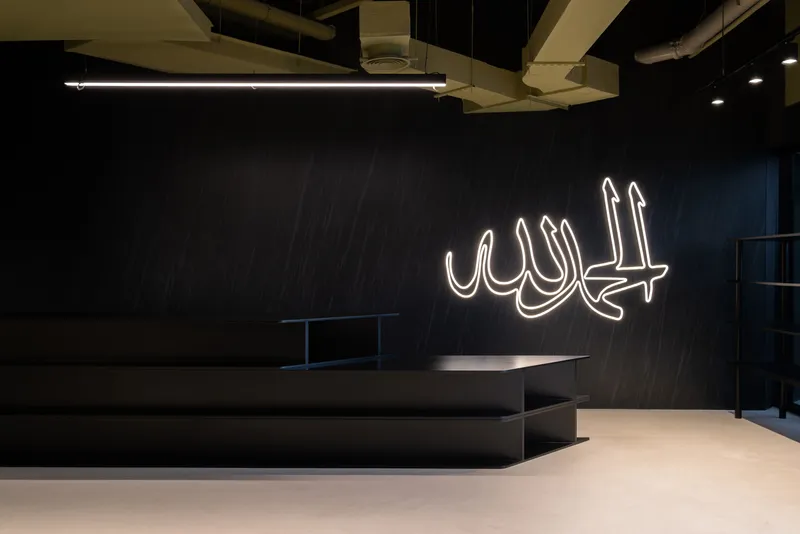 Dark feature wall with white neon Arabic calligraphy above low platform seating and polished concrete floor
