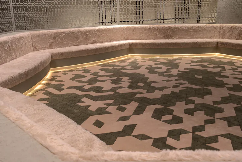 Sunken pool with geometric tiled pattern bordered by plush upholstered seating and perforated metal screens