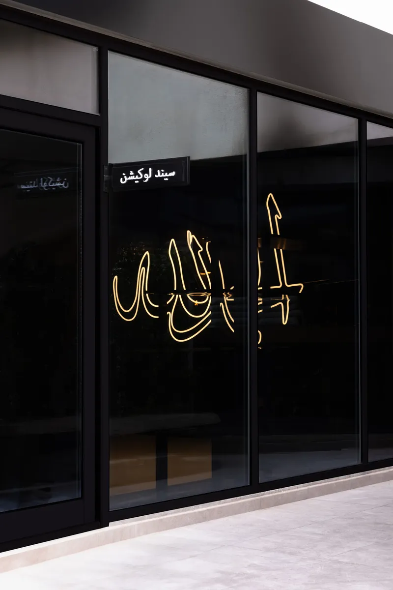 Storefront with illuminated calligraphic neon signage on black glass beneath transom windows