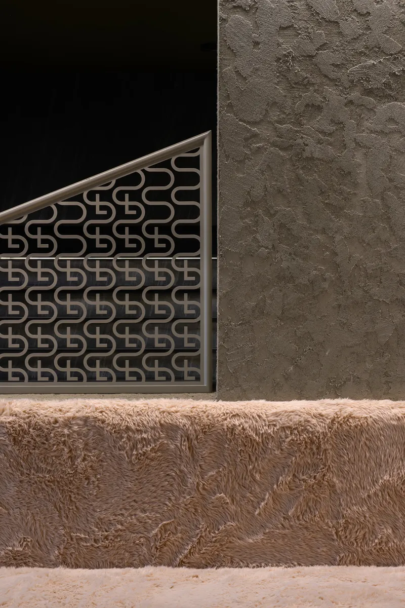 Corner detail of patterned metal screen against textured plaster wall above fur-covered base