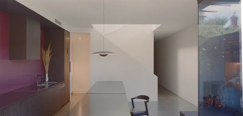 Kitchen with dark timber cabinetry and pendant light beside a white partition wall with curved shadow