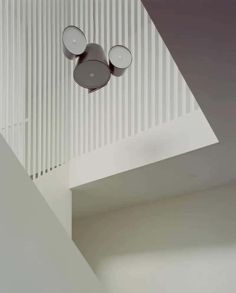 Looking up through stairwell void at cluster of three drum pendant lights against vertical rod railings