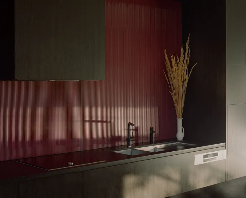 Kitchen counter with ribbed red glass backsplash and steel sink illuminated by natural light from above