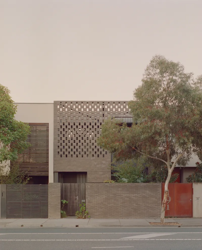 Street facade with perforated brick screen above a timber-slatted gate and planted boundary wall