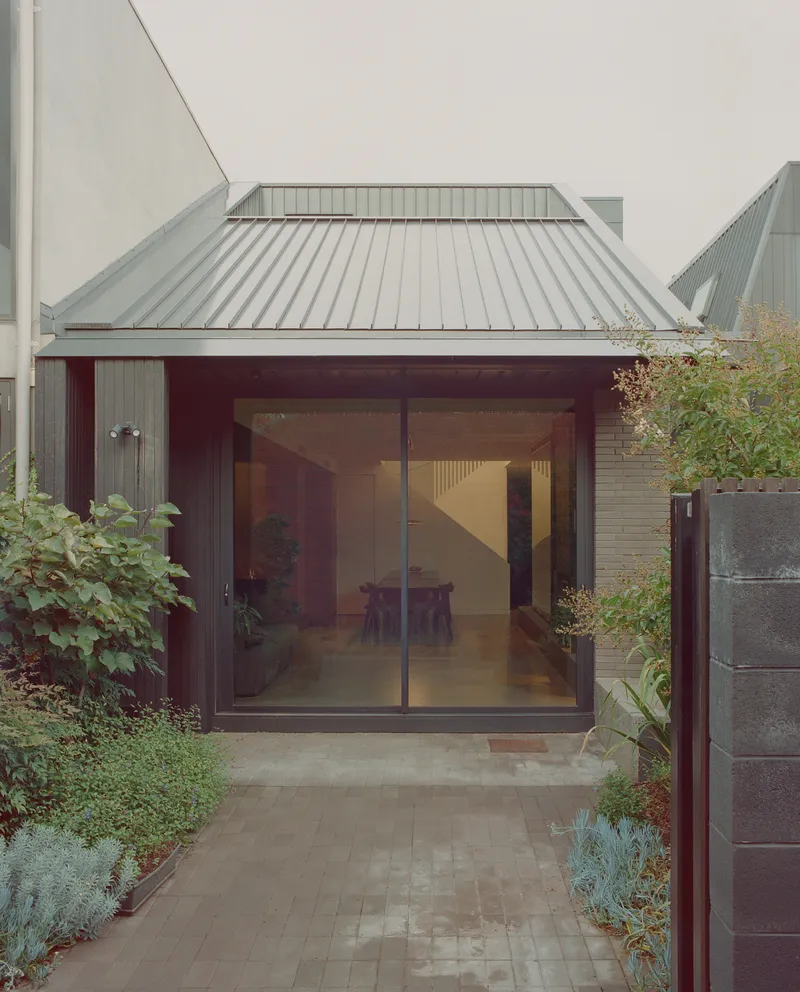 Courtyard entry with sliding glass doors under a standing-seam metal roof and garden planting
