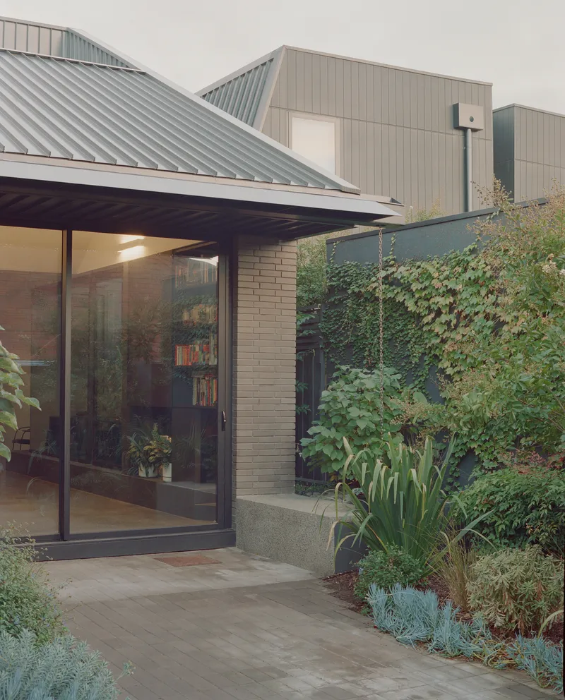 Covered entry with standing seam metal roof and glazed doors opening to planted beds with climbing vines
