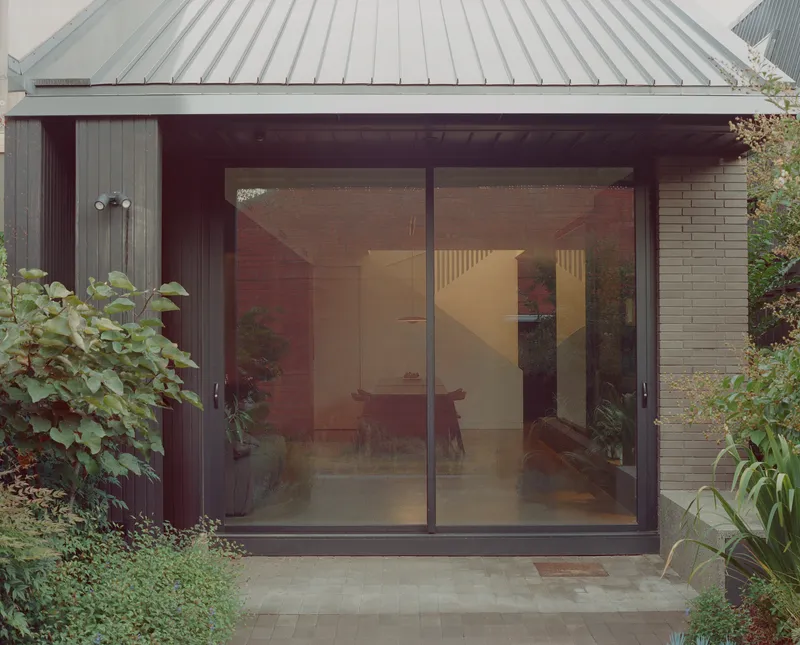 Glass sliding doors under a deep overhang framed by vertical timber cladding and beige brick