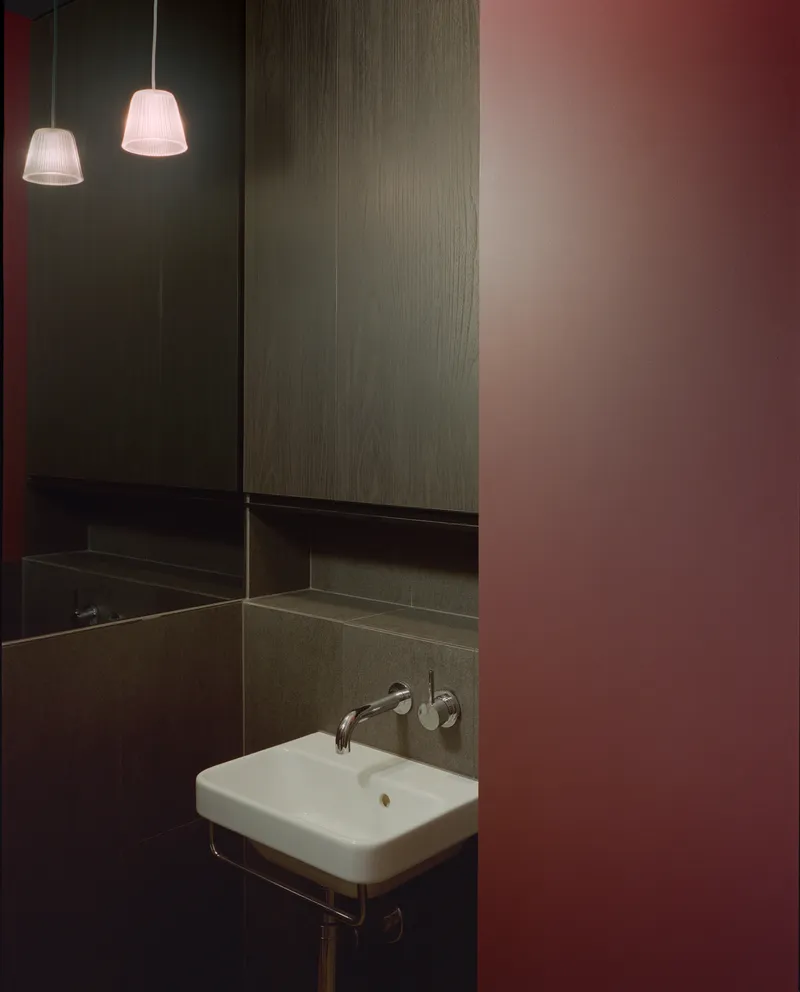 Wall-mounted basin beneath pendant lights framed by pink and timber-clad surfaces in powder room