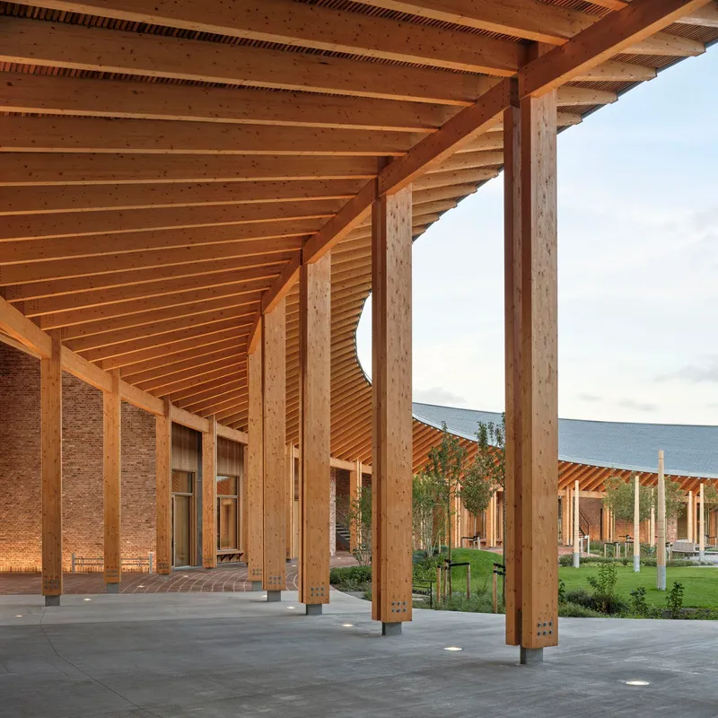 Detail of the timber colonnade with exposed ceiling joists and brick wall beneath overcast sky