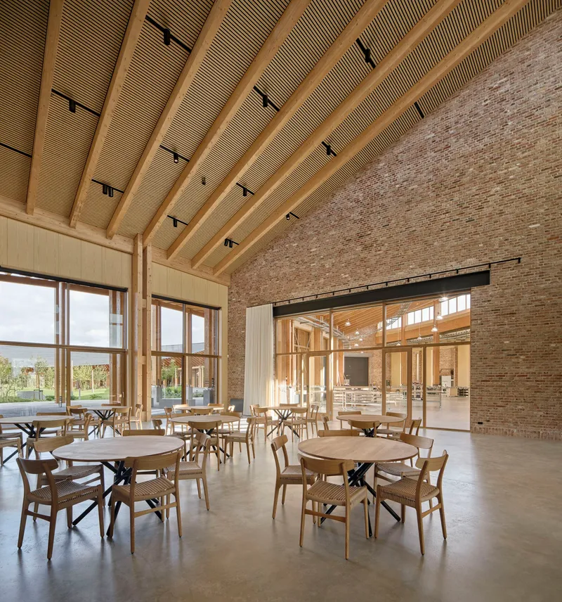 Dining hall interior with curved timber ceiling, brick wall and large windows overlooking the landscape