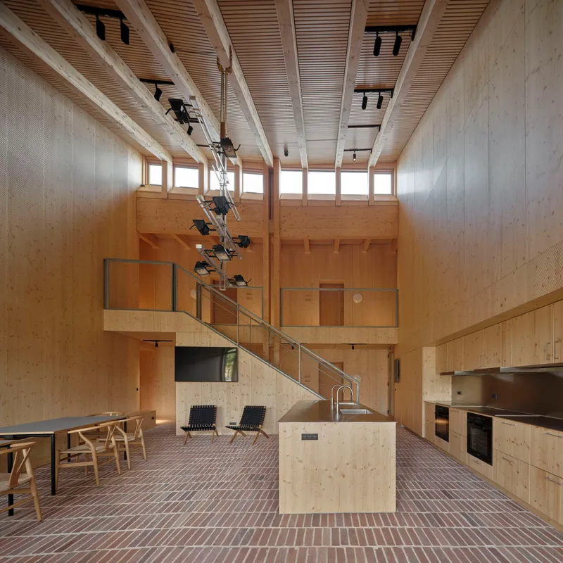 Double-height kitchen space with timber walls, mezzanine staircase and brick tile flooring throughout