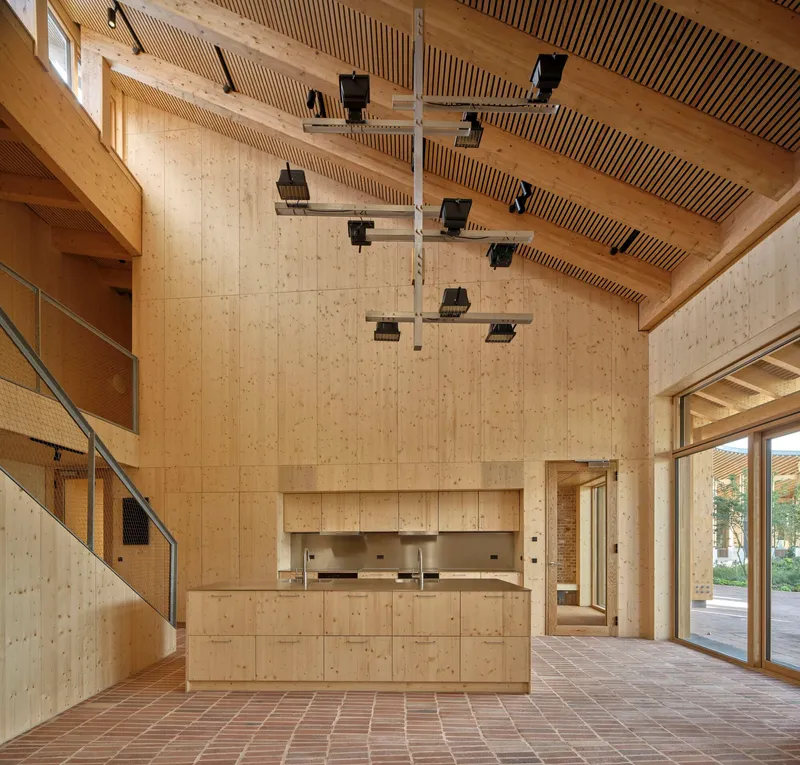 Interior foyer with cross-laminated timber walls, slatted ceiling, brick floor and suspended lighting fixtures