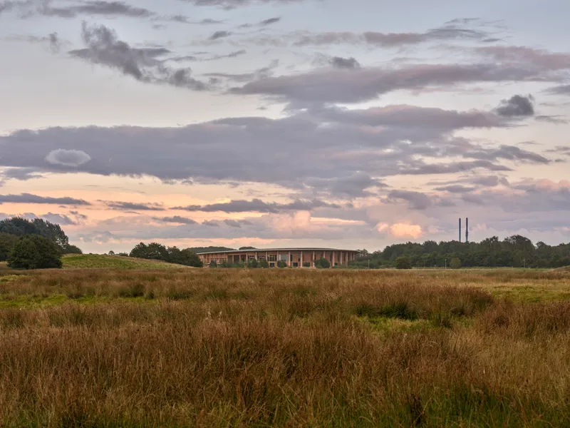 Distant view of the oval building across a wild meadow at dusk