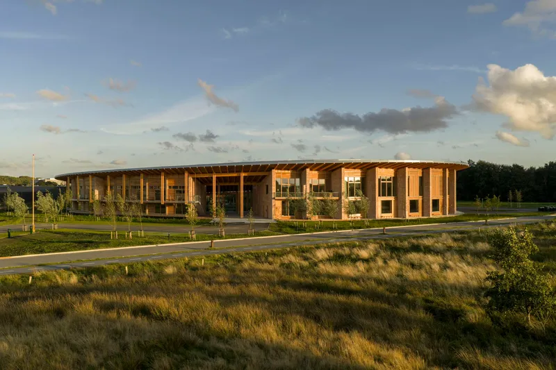 Timber colonnade and glazed facade viewed across native grasses at dusk