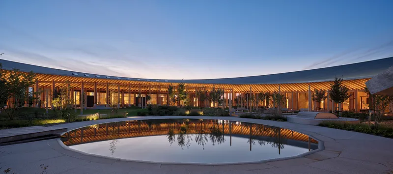 Circular reflecting pool with curved timber colonnade illuminated at twilight