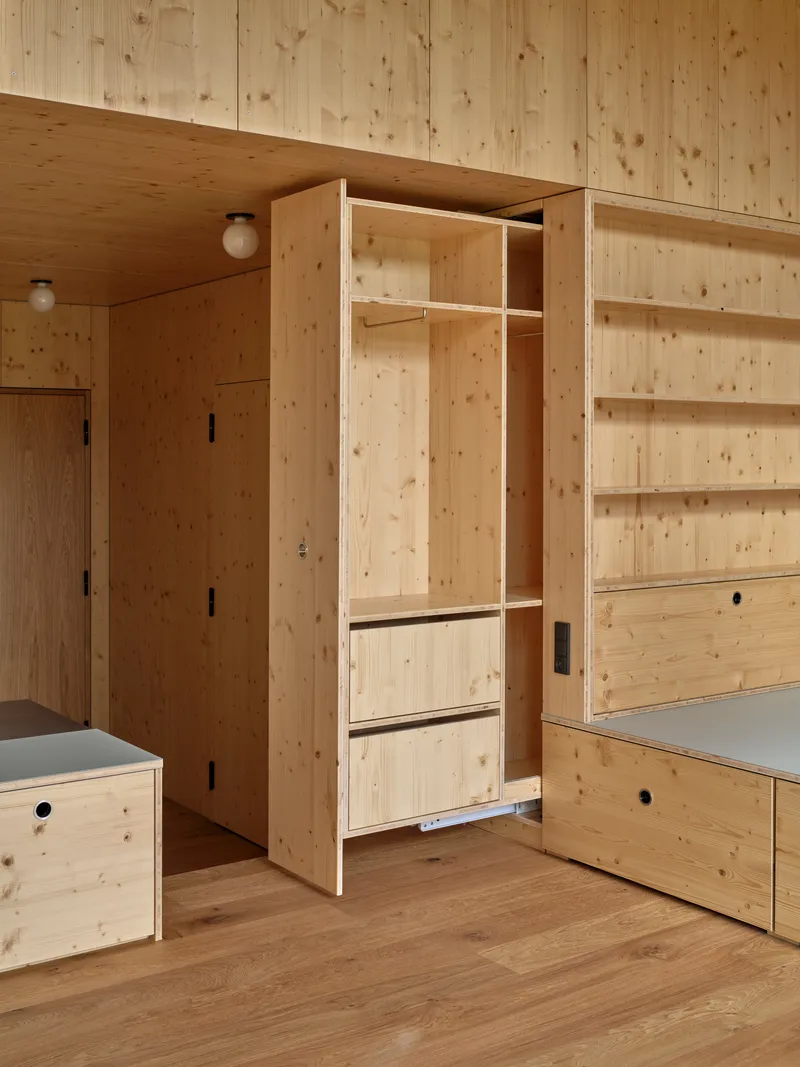 Open plywood wardrobe with hanging rail and drawers beside integrated shelving along the wall