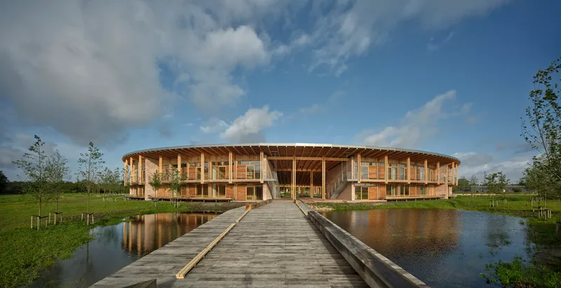 Timber boardwalk crossing a pond leading to the circular brick and timber structure