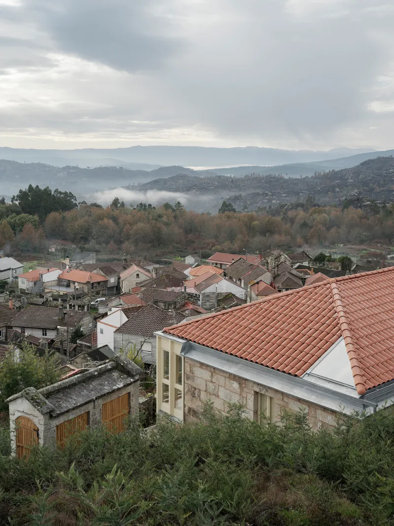 Terracotta roof among village houses with forested hills and low clouds in the distance
