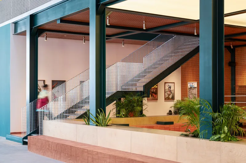Metal mesh staircase ascending behind planted concrete planters with perforated orange acoustic panels beyond