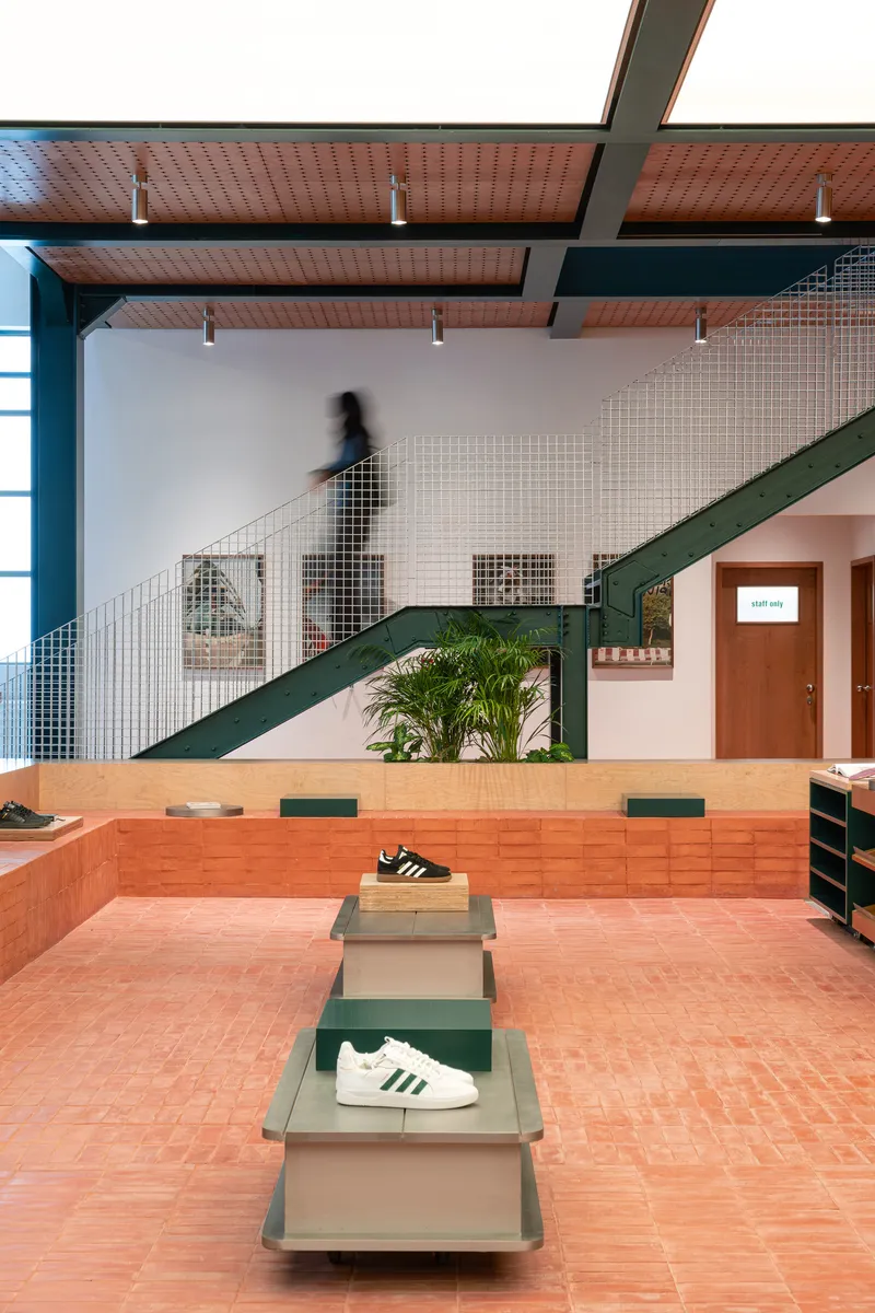 Interior retail space with terracotta floor, metal mesh staircase, and perforated ceiling with pendant lights