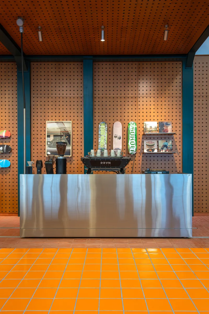 Polished stainless steel counter against perforated pegboard wall with terracotta tile floor and ceiling
