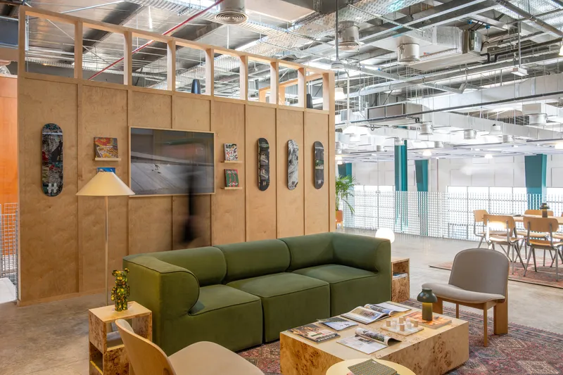 Plywood partition wall displaying skateboards and artwork with exposed ceiling infrastructure beyond