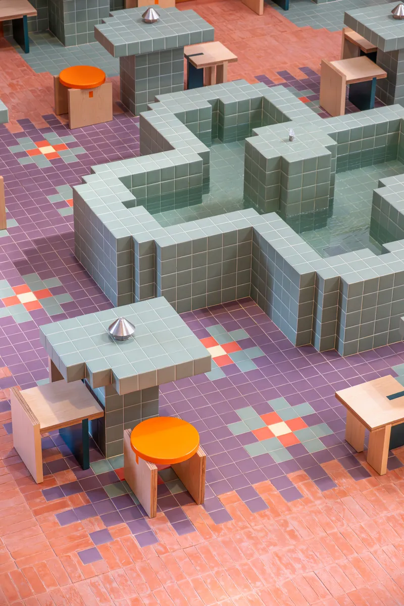 Overhead view of pixelated mosaic floor in purple and coral tones with tiled cubic volumes and orange seating