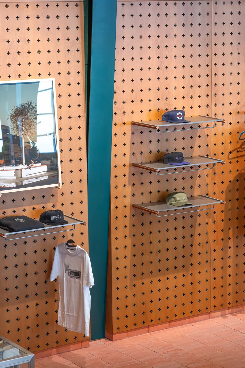 Perforated plywood wall with cross pattern holding glass shelves and merchandise near a storefront window