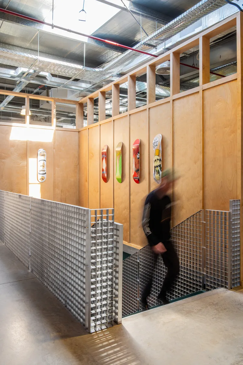 Timber-framed enclosure with perforated metal base and exposed ceiling ductwork as a person passes by