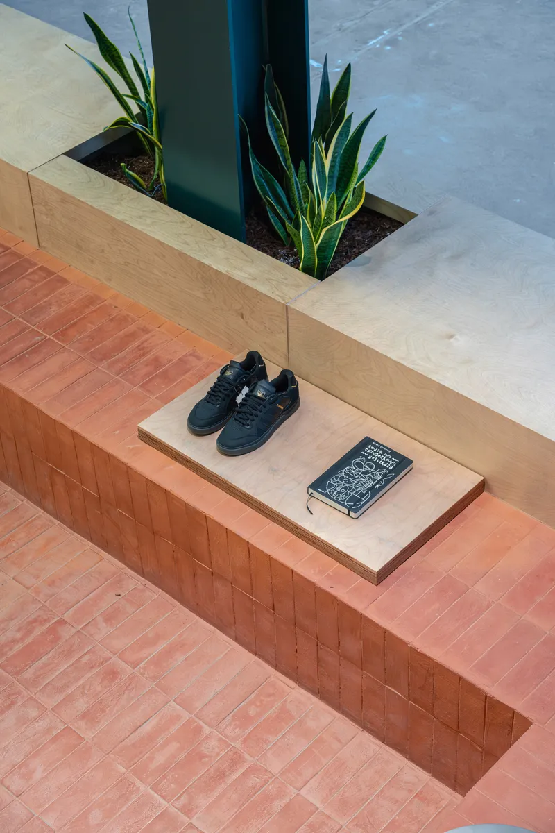 Stepped terracotta tile bench with planted steel column base and timber ledge under daylight