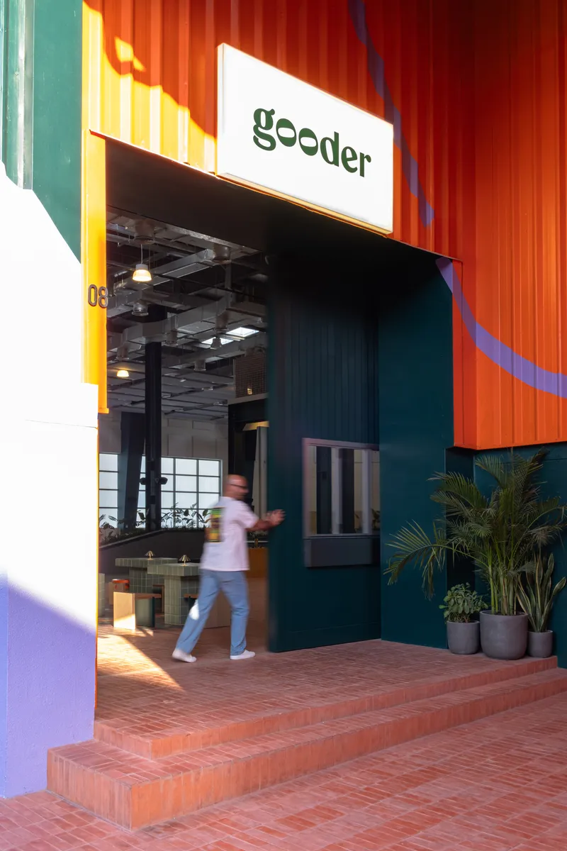 Entrance with corrugated orange metal facade and person walking through glazed doorway at dusk