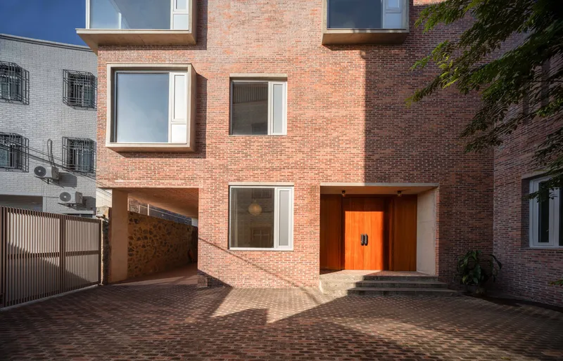 Red brick facade with recessed orange entry door and bay windows viewed from the brick-paved courtyard