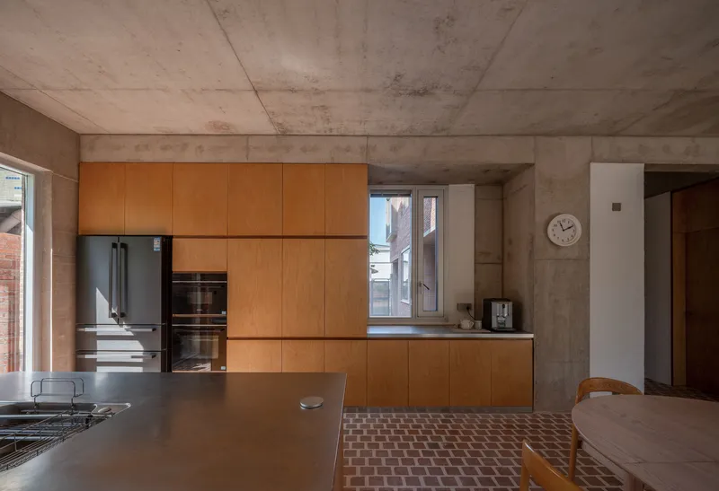 Kitchen with light wood cabinetry and exposed concrete ceiling above chequered brick floor